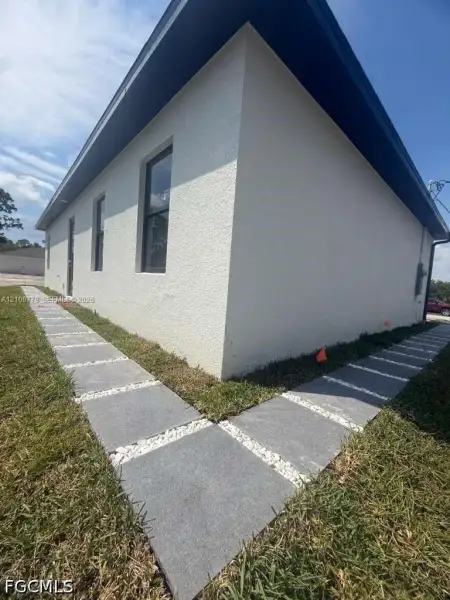 Stucco exterior featuring dark-trimmed windows, a deep roof overhang, and a modern paver walkway with decorative stone inlay Stucco exterior featuring dark-trimmed windows, a deep roof overhang, and a modern paver walkway with decorative stone inlay