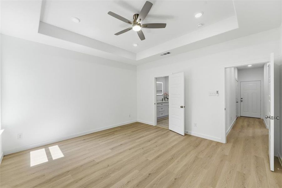 Spacious room featuring light wood-finish flooring, a tray ceiling with recessed lighting, and a modern ceiling fan