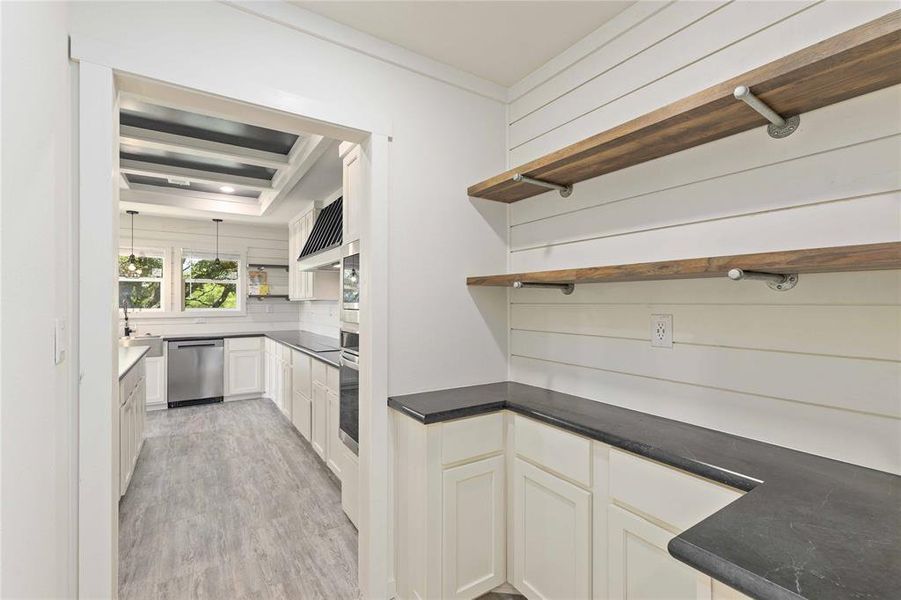 Pantry with shiplap accent wall, dark countertops, and open wood shelving