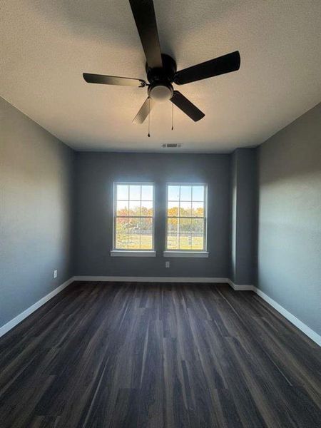 Empty room featuring a textured ceiling, dark wood finished floors, and a ceiling fan
