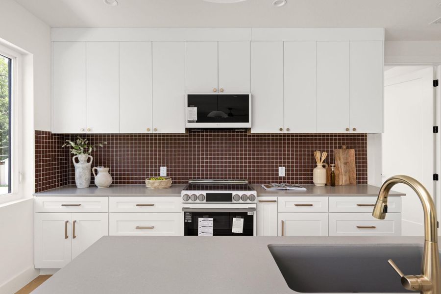 A sleek, modern kitchen offers ample counter space and pristine cabinetry with a stylish tiled backsplash. A sleek, modern kitchen offers ample counter space and pristine cabinetry with a stylish tiled backsplash.
