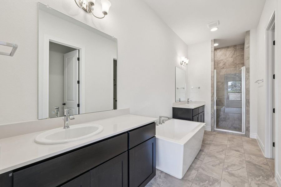 Full bath featuring two vanities, a freestanding bath, a shower stall, light marble finish floors, and recessed lighting