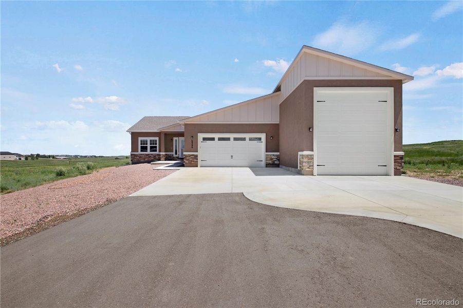 View of front of house featuring a garage, stone siding, concrete driveway, and stucco siding
