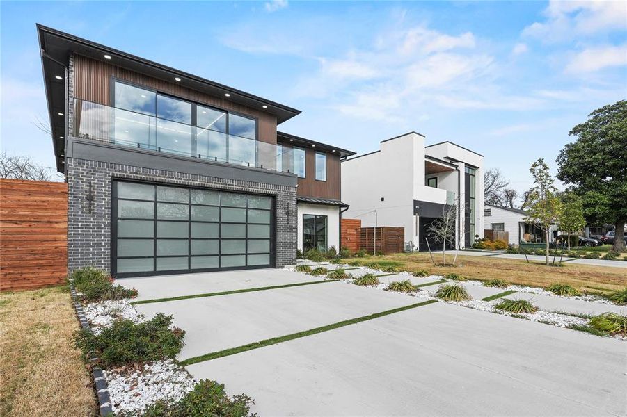 Contemporary home featuring concrete driveway, an attached garage, brick siding, and a balcony Contemporary home featuring concrete driveway, an attached garage, brick siding, and a balcony
