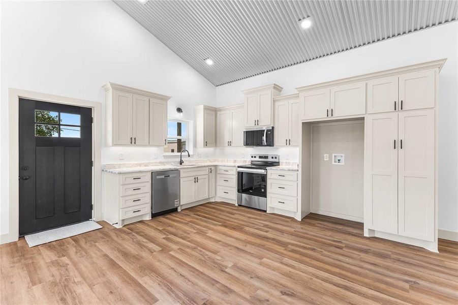 Kitchen with appliances with stainless steel finishes, high vaulted ceiling, plenty of natural light, light wood finished floors, and recessed lighting Kitchen with appliances with stainless steel finishes, high vaulted ceiling, plenty of natural light, light wood finished floors, and recessed lighting