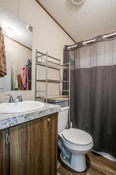 Bathroom featuring lofted ceiling, vanity, toilet, wood-type flooring, and a textured ceiling