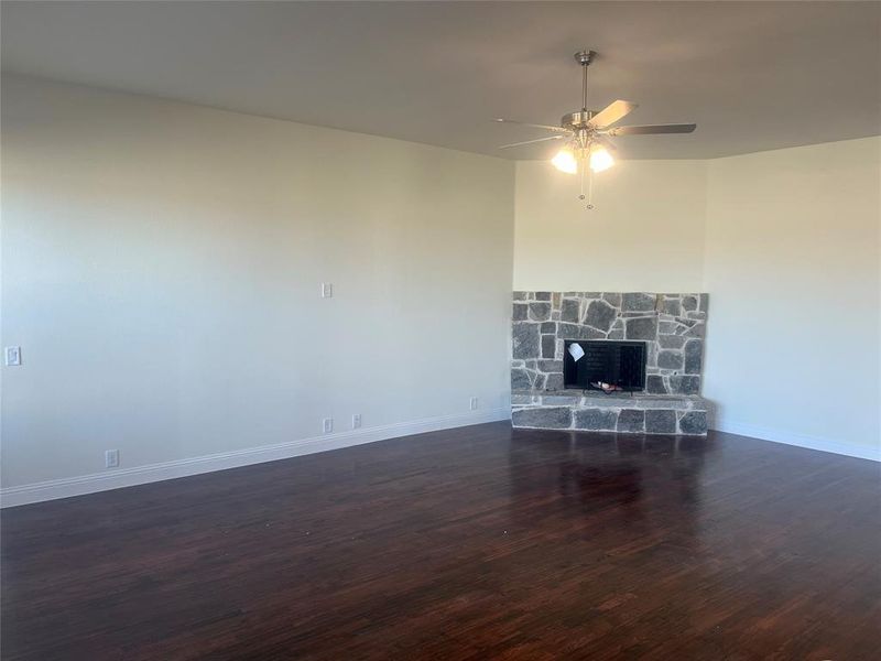 Unfurnished living room featuring a fireplace, dark wood-type flooring, and ceiling fan