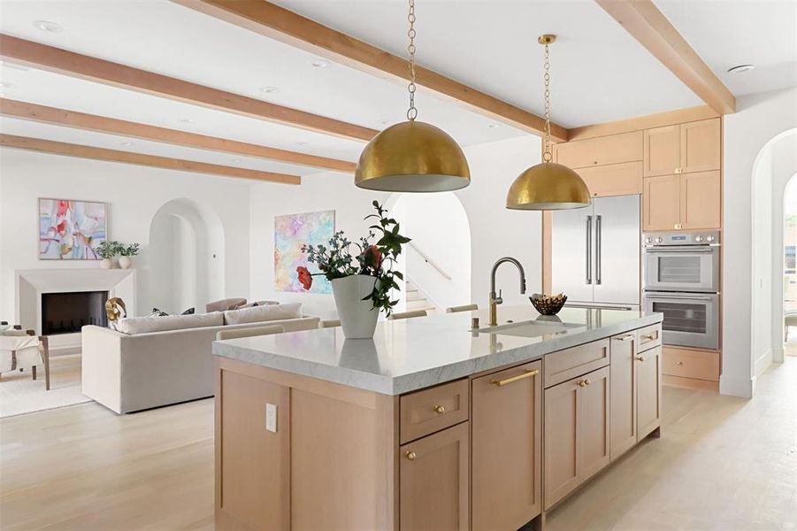 Kitchen with sink, stainless steel double oven, decorative light fixtures, beam ceiling, and a kitchen island with sink