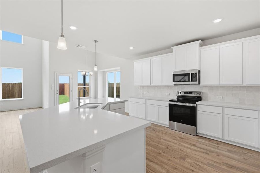 Open-concept kitchen featuring an expansive island with a sink, white cabinetry, a subway tile backsplash, and stainless steel appliances