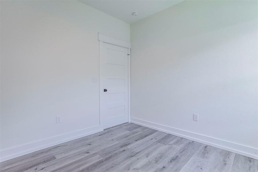 Interior room featuring light gray wood-finish flooring, white walls, and a white paneled door with black hardware