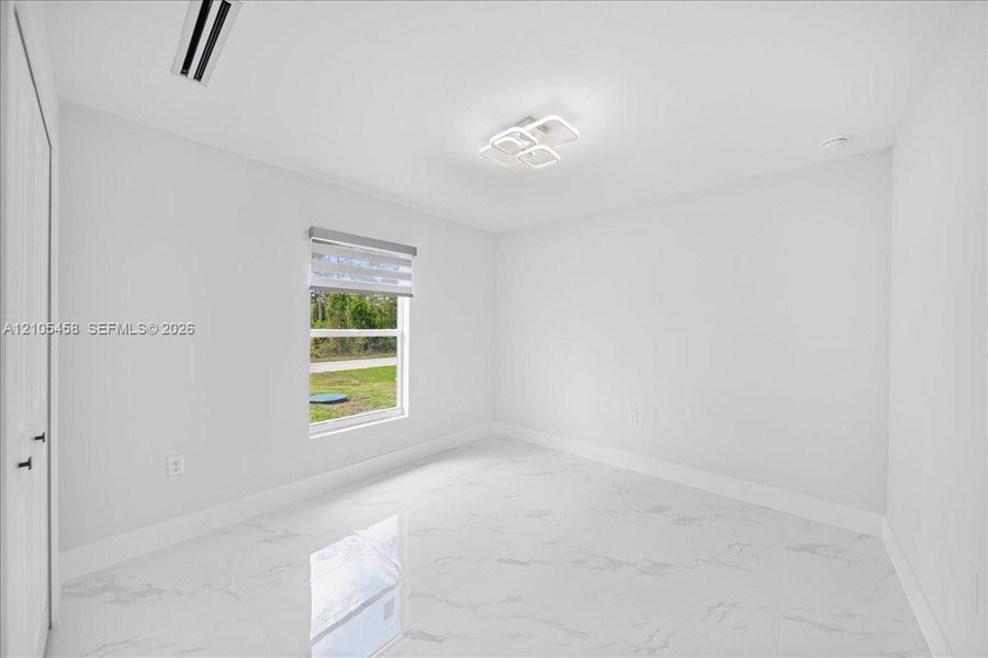White tile flooring, modern ceiling light fixture, single window with blinds, white walls, and a white door with black hardware White tile flooring, modern ceiling light fixture, single window with blinds, white walls, and a white door with black hardware