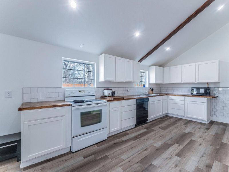 Kitchen with butcher block countertops, electric range, lofted ceiling, tasteful backsplash, and white cabinets