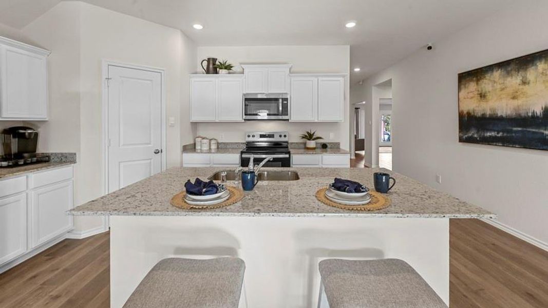 Kitchen featuring white cabinets, stainless steel appliances, light stone countertops, a kitchen bar, and dark wood-style floors