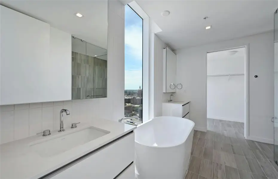 Experience elevated luxury in this stunning primary bathroom featuring sleek, modern design and panoramic views of the Texas State Capitol. A deep soaking tub invites relaxation beside floor-to-ceiling windows that bathe the space in natural light. Clean lines, contemporary vanities with ample storage, and sophisticated tilework create a serene, spa-like retreat in the heart of downtown Austin.