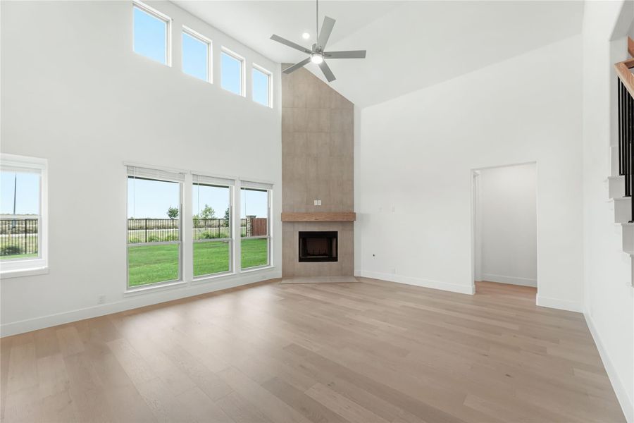 Open living room with two-story ceiling, tile fireplace, ceiling fan, and light hardwood floors