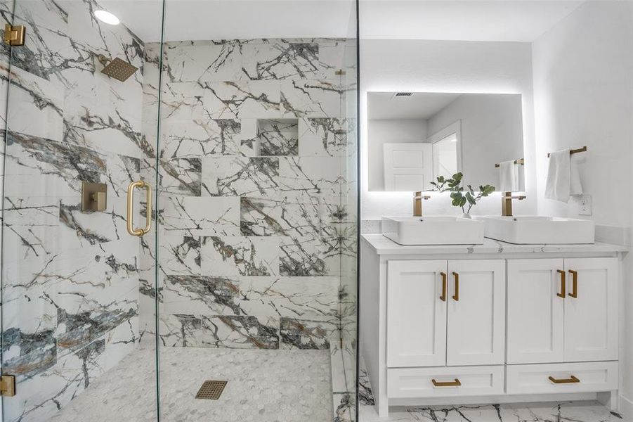 Full bathroom with a marble finish shower, double vanity, and light marble finish floors Full bathroom with a marble finish shower, double vanity, and light marble finish floors