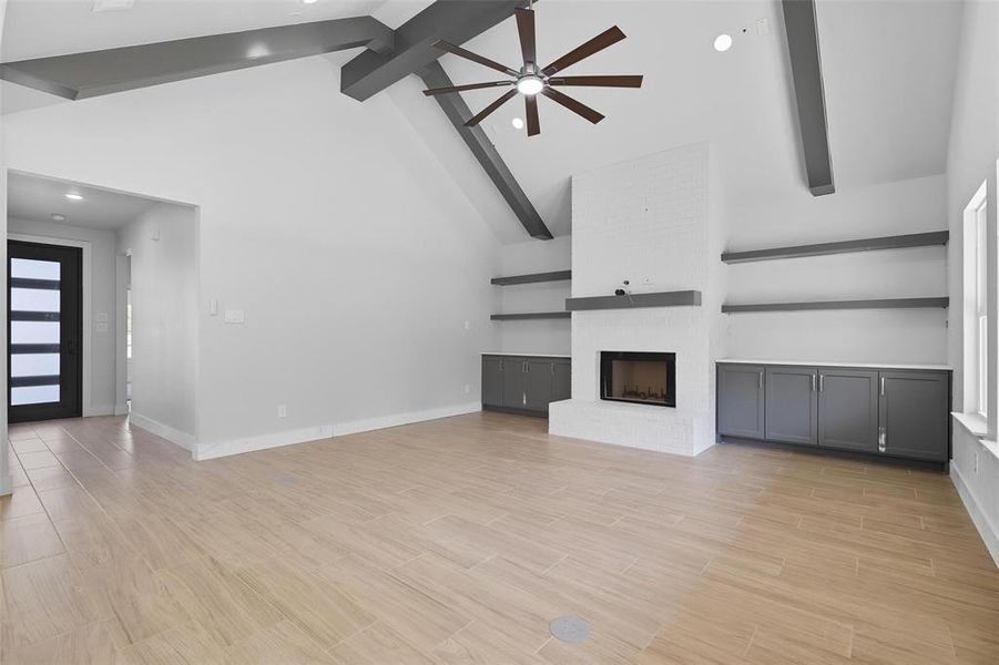 Unfurnished living room featuring beam ceiling, high vaulted ceiling, wood tiled floors, a brick fireplace, and recessed lighting Unfurnished living room featuring beam ceiling, high vaulted ceiling, wood tiled floors, a brick fireplace, and recessed lighting