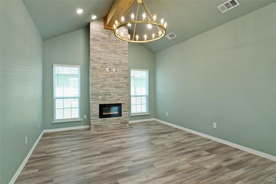 Unfurnished living room with a tile fireplace, a wealth of natural light, beamed ceiling, and a chandelier