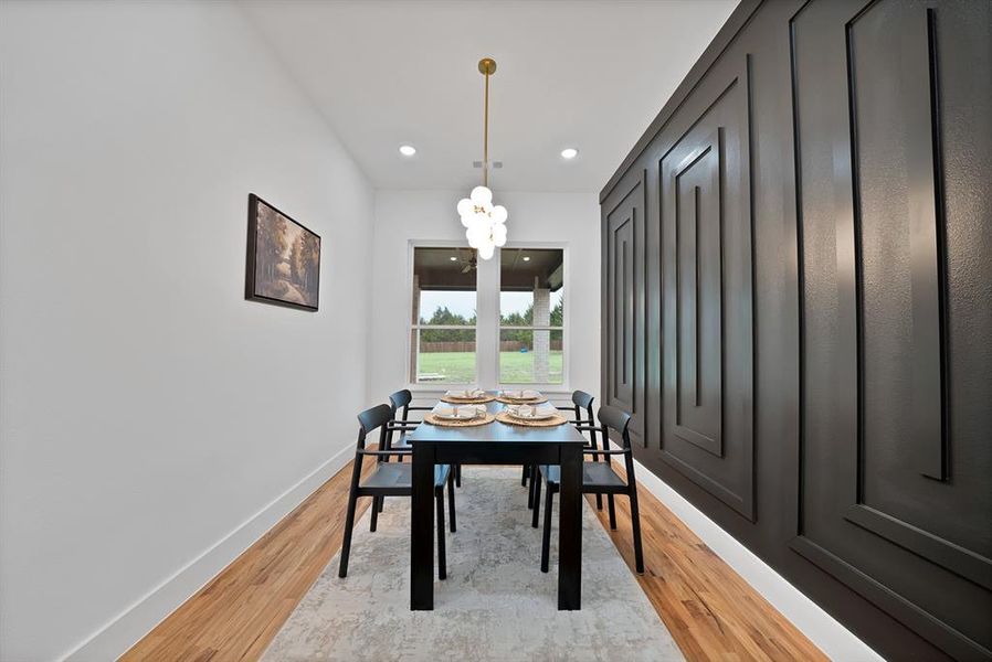 Dining area featuring hardwood flooring, a decorative accent wall with geometric paneling, and a contemporary chandelier