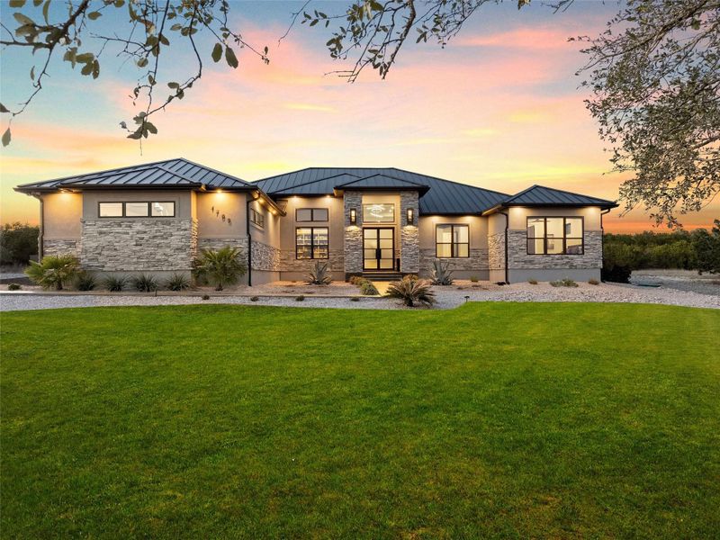 Front view of house featuring stone siding, a standing seam roof, a yard, and stucco siding