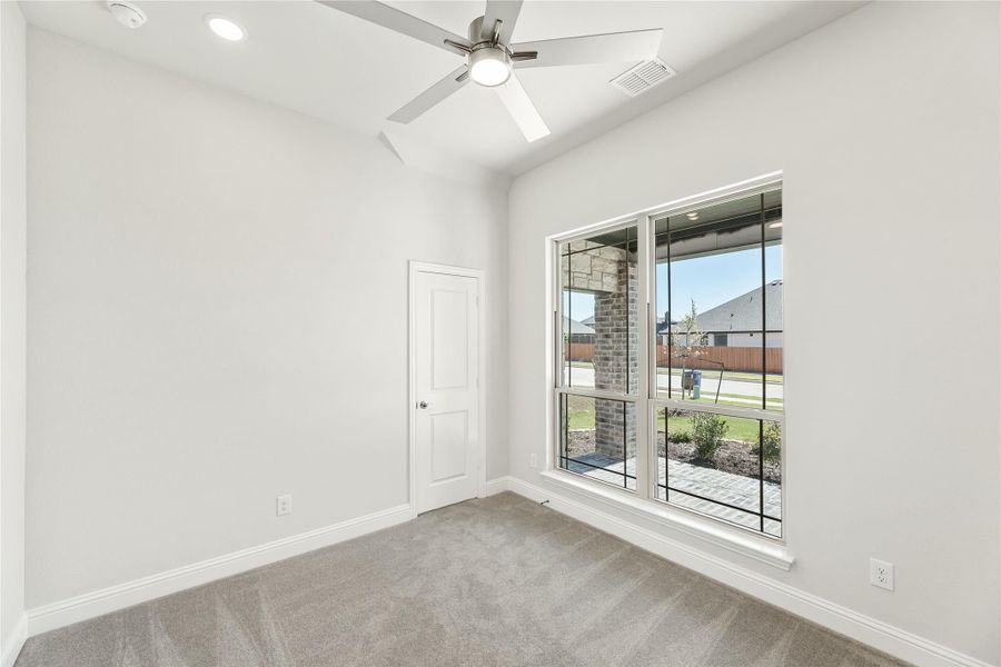 Empty bedroom with gray carpet, ceiling fan, and large window overlooking backyard patio