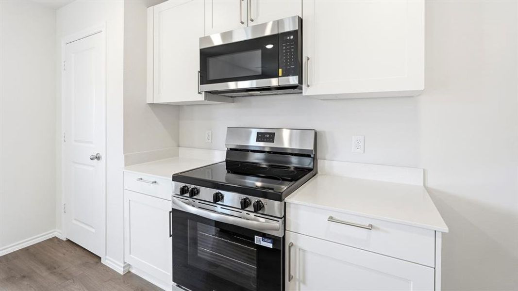 Kitchen with stainless steel appliances, white cabinetry, light countertops, and dark wood-style floors
