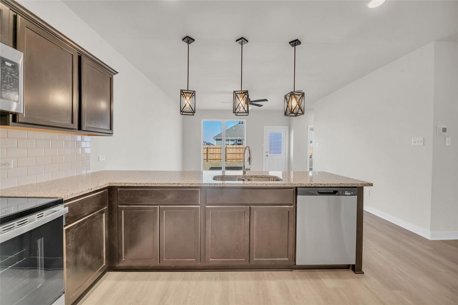 Kitchen featuring light stone countertops, a sink, stainless steel appliances, dark brown cabinetry, and backsplash