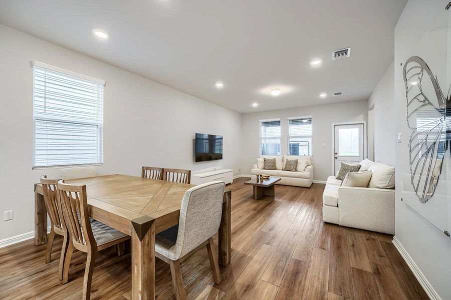 Open-concept living area featuring wood-finish flooring, recessed lighting, and multiple windows with blinds