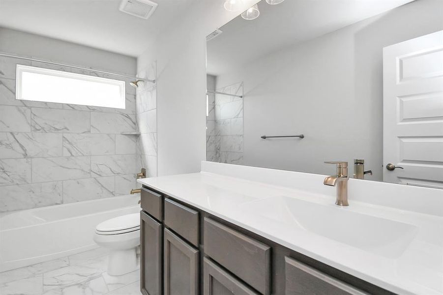 The secondary bath boasts stylish tile flooring, a bath/shower combo with a sleek tile surround, light wood cabinets, and a stunning light countertop.