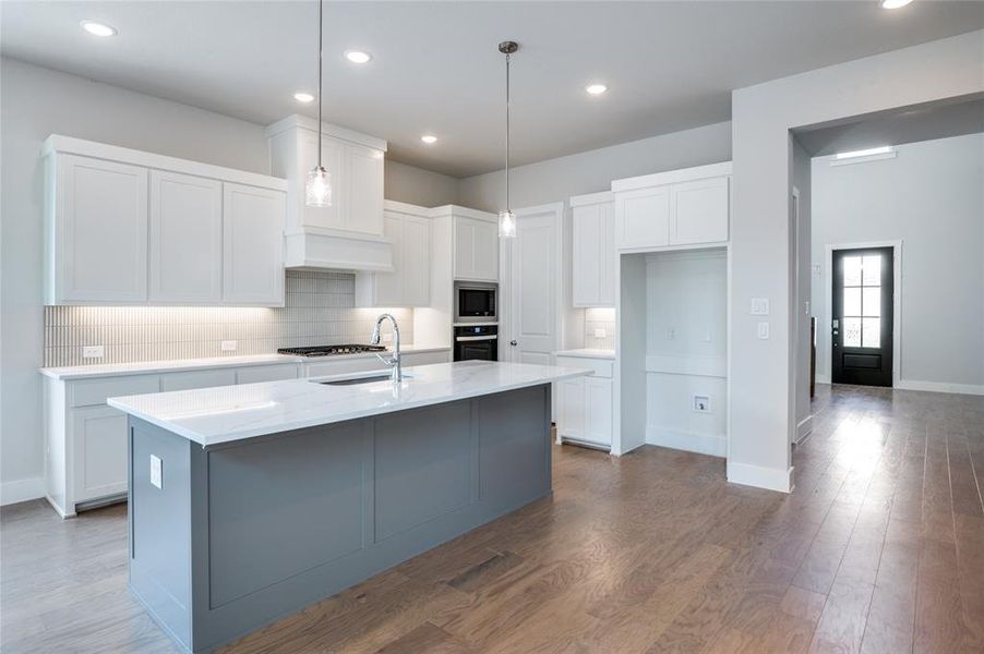 Kitchen with appliances with stainless steel finishes, backsplash, hardwood / wood-style floors, an island with sink, and white cabinets