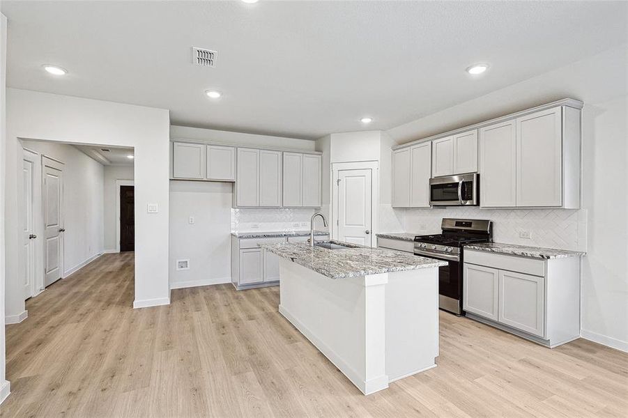 Kitchen featuring appliances with stainless steel finishes, a center island with sink, light stone countertops, and light hardwood / wood-style floors