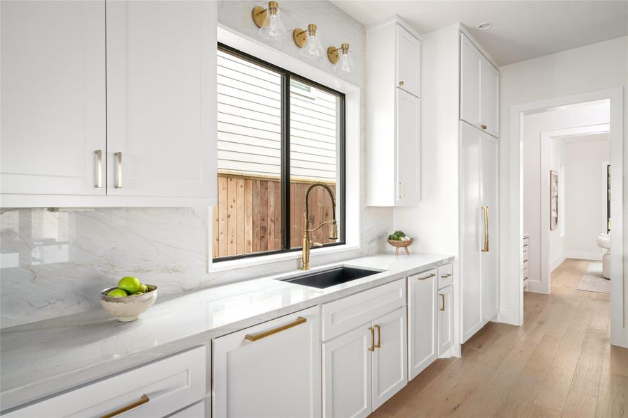 Bright and functional workspace featuring a sleek black undercount sink, brushed brass faucet, and full height marble backsplash. Surrounded by custom white cabinetry and expansive counter space, this area blends everyday function with elegant design. Bright and functional workspace featuring a sleek black undercount sink, brushed brass faucet, and full height marble backsplash. Surrounded by custom white cabinetry and expansive counter space, this area blends everyday function with elegant design.