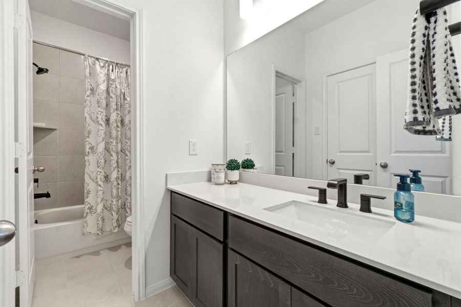 Modern bathroom featuring a sleek double vanity with dark cabinets and black fixtures. The space includes a well-lit mirror, and a separate shower/tub area with a decorative curtain, offering both style and functionality.