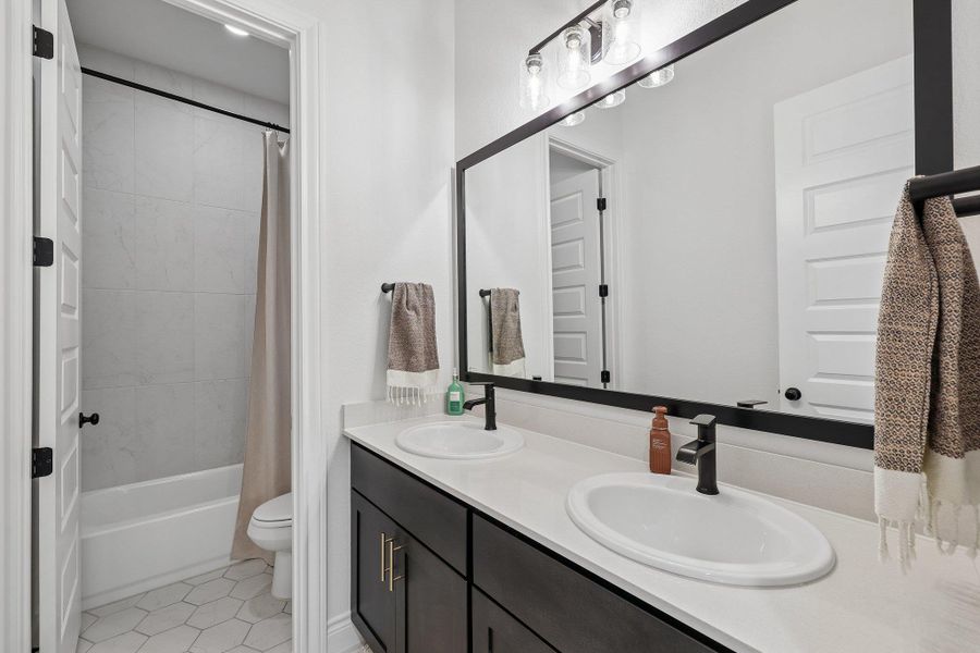 Bathroom featuring a dual vanity with white countertops and dark cabinetry, matte black hardware, a large framed mirror, and a tub-shower combination with white subway tile surround