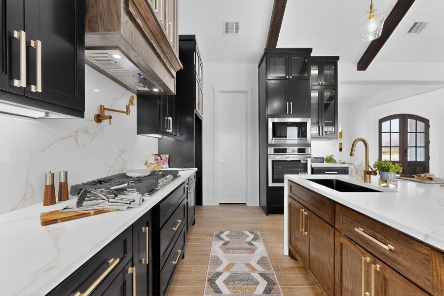 Kitchen featuring dark cabinetry, glass insert cabinets, light stone counters, stainless steel appliances, and wood finish floors