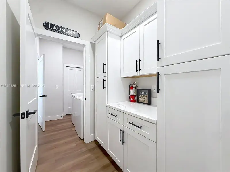 Custom white cabinetry featuring shaker-style doors, matte black hardware, and light-toned composite countertops, complemented by wood-finish flooring