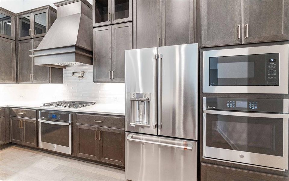 Gourmet kitchen showcasing stainless steel appliances, dark wood-finish cabinetry, white countertops, and a subway tile backsplash Gourmet kitchen showcasing stainless steel appliances, dark wood-finish cabinetry, white countertops, and a subway tile backsplash