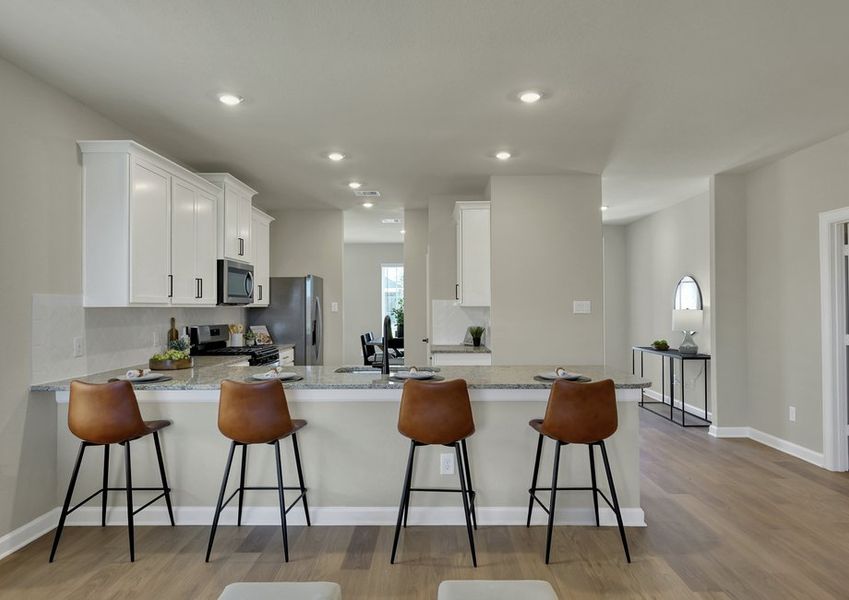 Open-concept kitchen and living area featuring a granite island with bar seating, white cabinetry, and stainless appliances.