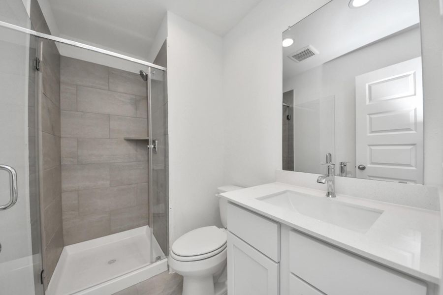 Secondary bath features tile flooring, walk-in shower with tile surround, light stained wood cabinets, beautiful light countertop. Sample photo of completed home with similar floor plan. Actual colors and selections may vary.