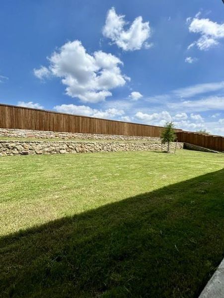 Expansive backyard featuring a lush lawn, a mature wood privacy fence, and a decorative stone retaining wall Expansive backyard featuring a lush lawn, a mature wood privacy fence, and a decorative stone retaining wall