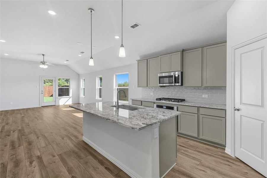 Kitchen featuring gray cabinets, tasteful backsplash, light stone countertops, decorative light fixtures, and lofted ceiling Kitchen featuring gray cabinets, tasteful backsplash, light stone countertops, decorative light fixtures, and lofted ceiling