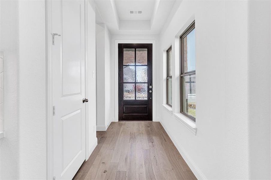 Doorway with a tray ceiling and light hardwood / wood-style floors