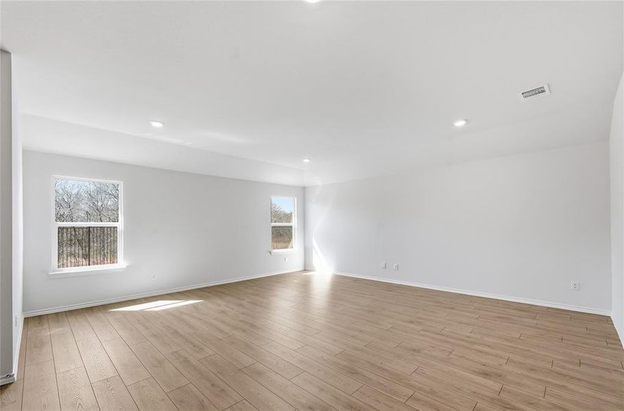 Spacious interior room featuring light wood-finish flooring, recessed lighting, and multiple windows providing natural illumination Spacious interior room featuring light wood-finish flooring, recessed lighting, and multiple windows providing natural illumination