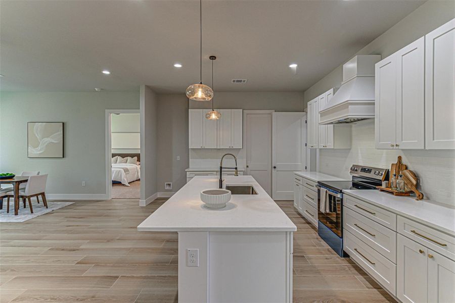 Kitchen with electric stove, premium range hood, basin sink, recessed lighting, and quartz countertops.