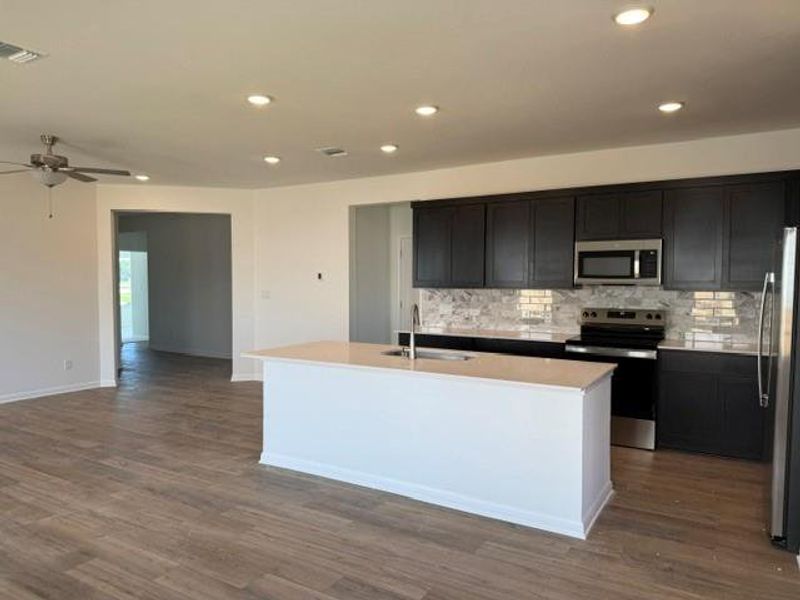 Open-concept kitchen featuring an island with sink, dark cabinetry, stainless steel appliances, and a tile backsplash Open-concept kitchen featuring an island with sink, dark cabinetry, stainless steel appliances, and a tile backsplash