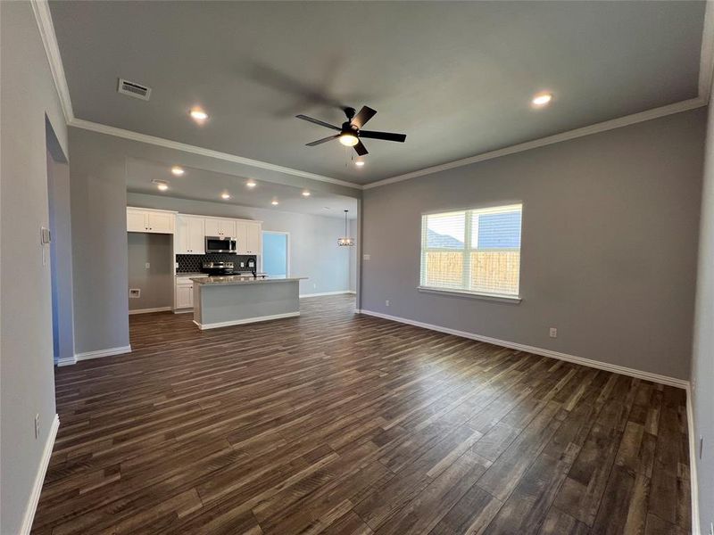 Unfurnished living room with crown molding, ceiling fan, and dark wood-type flooring