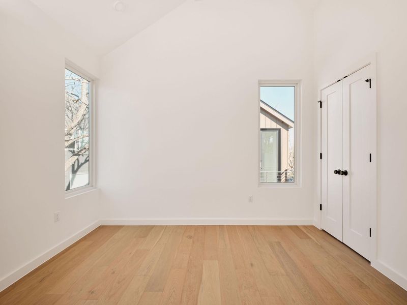 Unfurnished bedroom featuring light wood-style floors, multiple windows, a closet, and vaulted ceiling