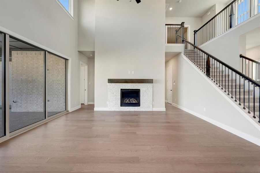 Unfurnished living room featuring light wood-style floors, a fireplace, a high ceiling, and recessed lighting Unfurnished living room featuring light wood-style floors, a fireplace, a high ceiling, and recessed lighting