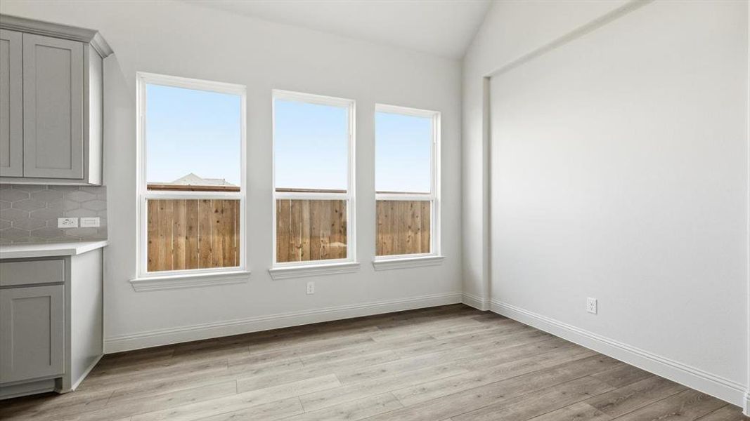 Bright interior space featuring three large windows, a wood-finish floor, and vaulted ceilings