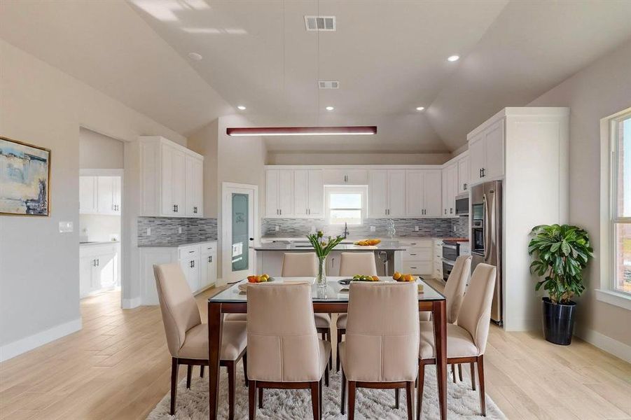 Dining area with light wood-type flooring, visible vents, baseboards, and vaulted ceiling